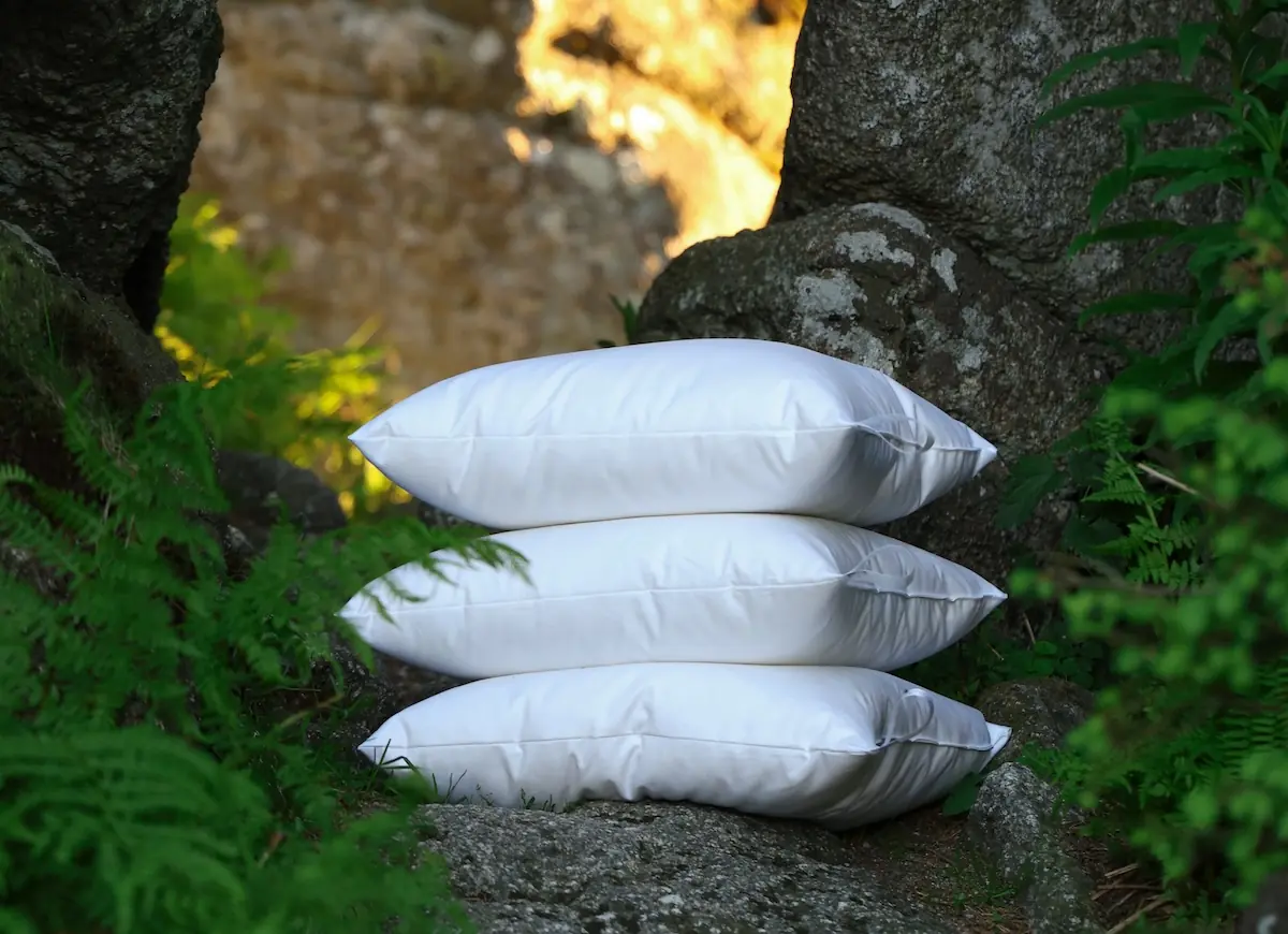 Three white pillows stacked on natural stone displaying softness and quality craftsmanship