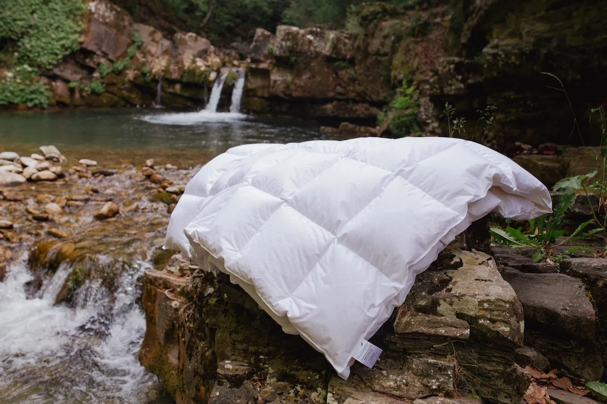White hypoallergenic duvet displayed on stone ledge beside natural waterfall