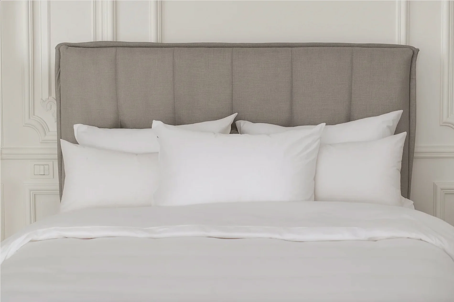 White duvet covers and pillows arranged on gray upholstered bed in elegant bedroom