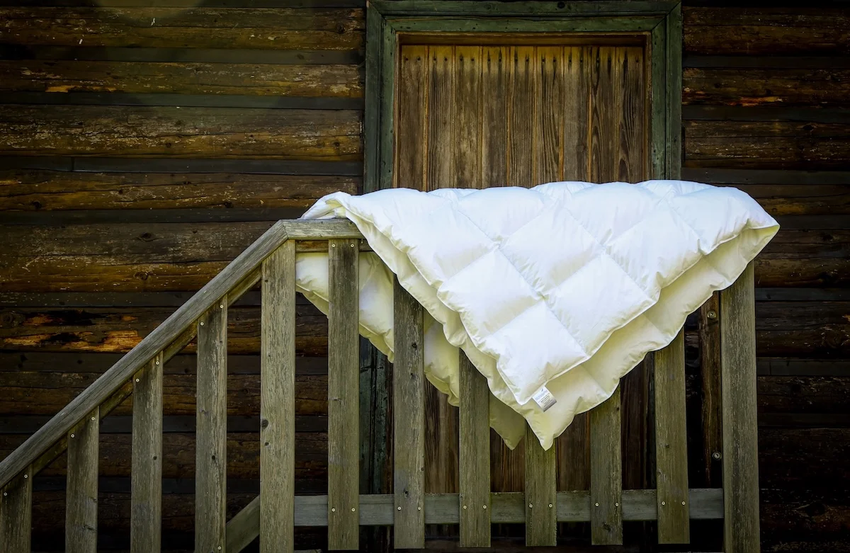 White winter duvet with yellow trim hanging on wooden cabin balcony