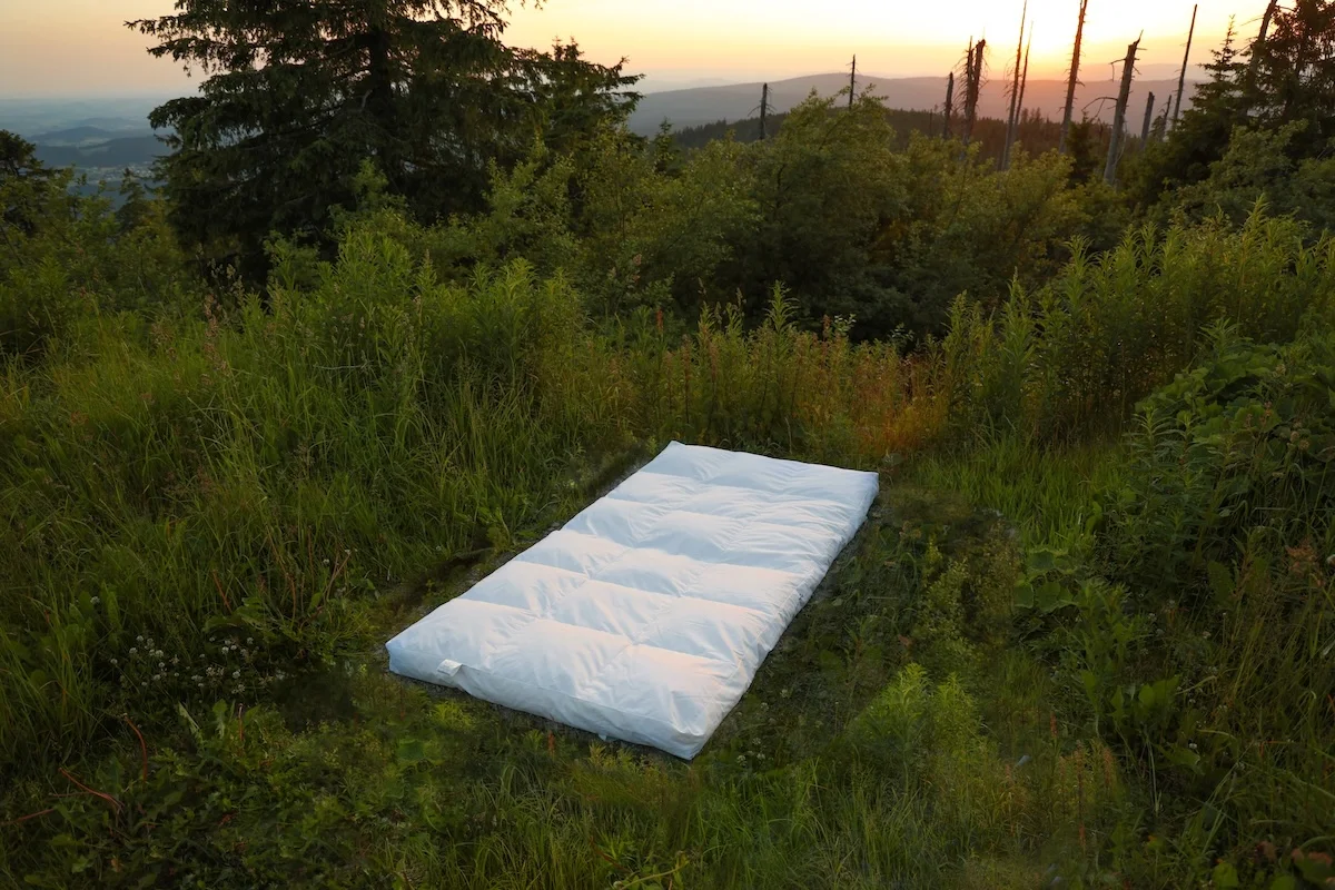 White mattress topper placed on grass in forest clearing at sunset