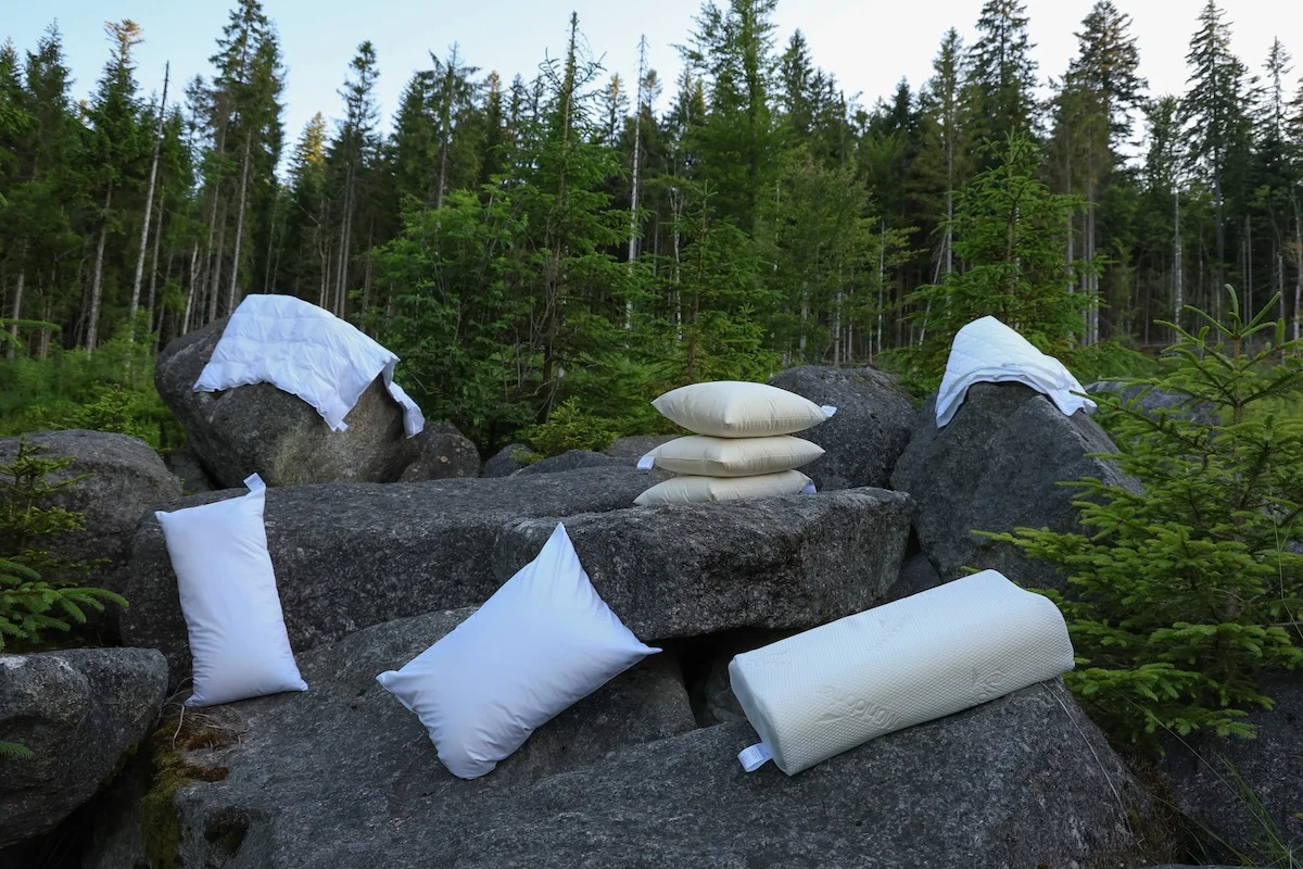Collection of white pillows and duvets arranged on forest rocks showcasing pillow variety