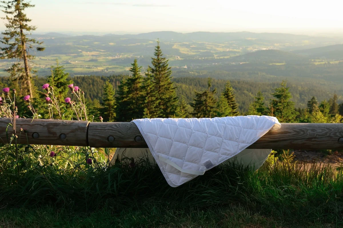 White quilted mattress pad on wooden fence overlooking mountain valley landscape