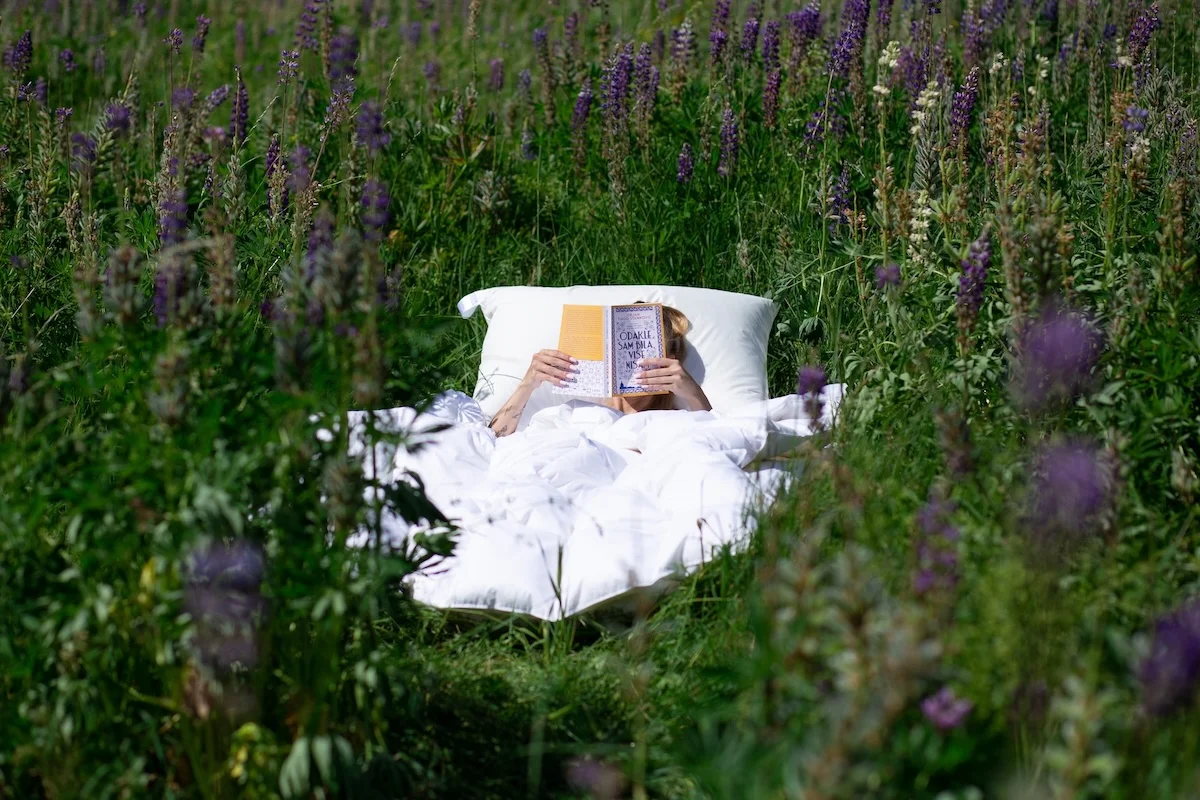 Person reading under white summer duvet in wildflower meadow