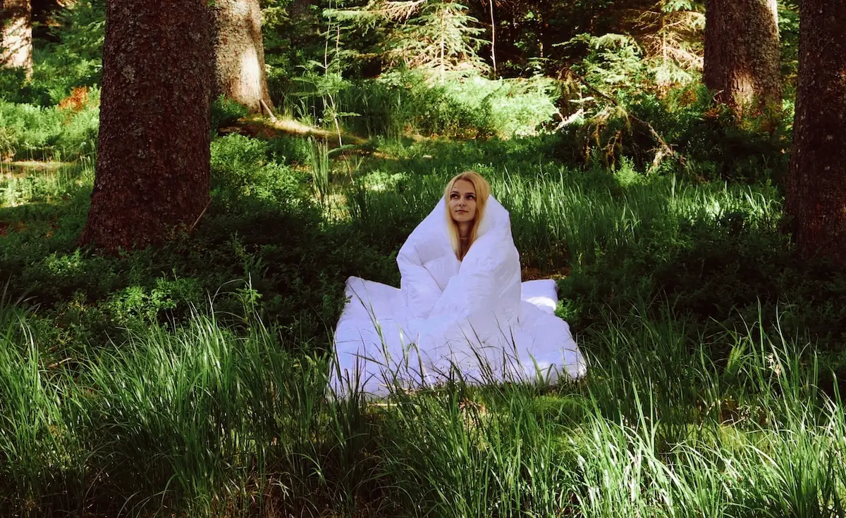 Woman wrapped in white down duvet in forest setting demonstrating warmth and coziness