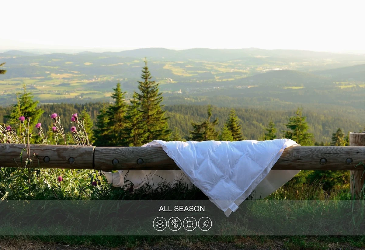 All-season white duvet hanging on wooden fence with mountain landscape and seasonal icons